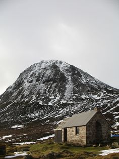 an old stone building in front of a snow - covered mountain with a metal roof