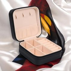 an open black and white box with compartments on it sitting on a satin surface next to a banana