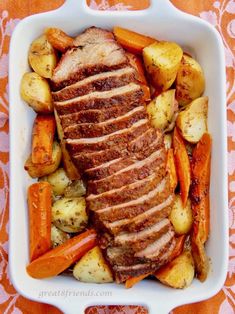 sliced pork, potatoes and carrots in a white casserole dish on an orange tablecloth