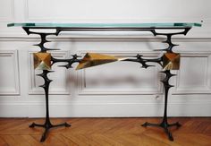 a glass topped table with metal legs and two birds on it's legs, in front of a white wall