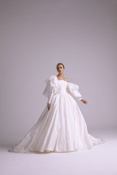 a woman in a white wedding dress with long sleeves and ruffles on the shoulders