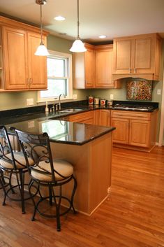 a kitchen with wooden cabinets and black counter tops on hard wood flooring next to an island that has four bar stools