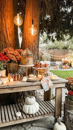 an outdoor table with candles, pumpkins and other decorations on it in front of a tree