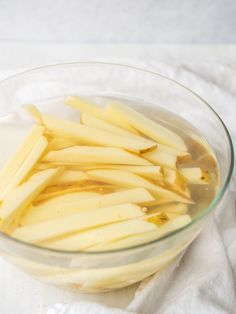 a glass bowl filled with sliced potatoes on top of a white cloth