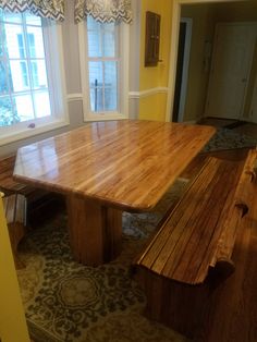 a large wooden table and bench in a room with yellow walls, patterned flooring and windows