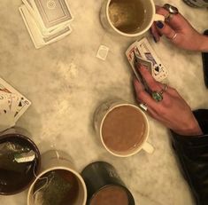 three cups of coffee are sitting on a table with playing cards in front of them