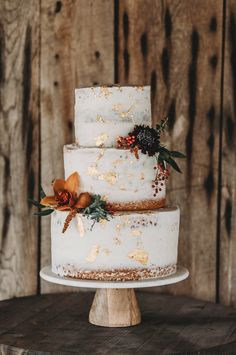 a three tiered white cake with flowers on the top is sitting on a wooden table