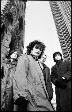 black and white photograph of four people standing in front of tall buildings with one person looking at the camera