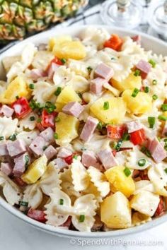 pasta salad with ham and pineapples in a white bowl on a marble table