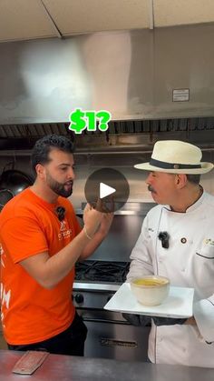 two men standing in a kitchen talking to each other while holding plates with food on them