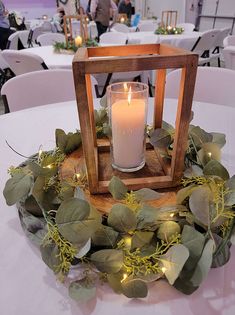 a candle is lit in a wooden lantern surrounded by greenery on a round table