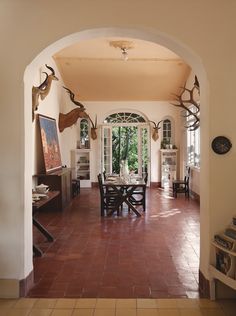 an archway leads into a dining room with deer heads on the wall and tile flooring