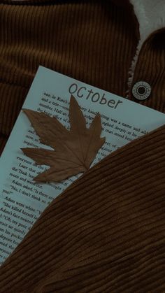 a leaf laying on top of an open book with the word october next to it