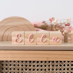 wooden blocks spelling the word'ella'on top of a table with flowers in the background