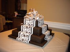 a three tiered cake with white and brown designs on it's sides sitting on a table