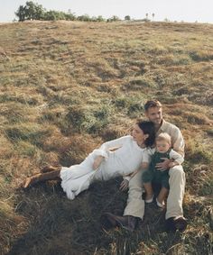 a man, woman and child sitting on the ground in a field with dry grass