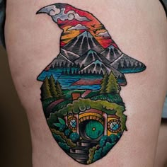 a colorful tattoo on the thigh of a woman with mountains and trees in the background