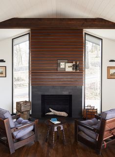 a living room with two chairs and a fire place in front of a window that has wood slats on the wall