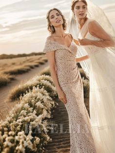 two women in wedding gowns standing next to each other on the beach, one wearing a veil