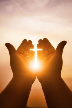 two hands holding a cross in front of the sun with their palms outstretched to it