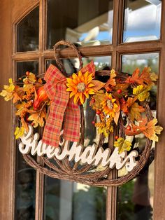 a wreath with the word thanksgiving written on it hanging from a front door, decorated with fall leaves and sunflowers