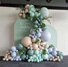 a birthday cake with balloons and greenery on the top is decorated in pastel colors