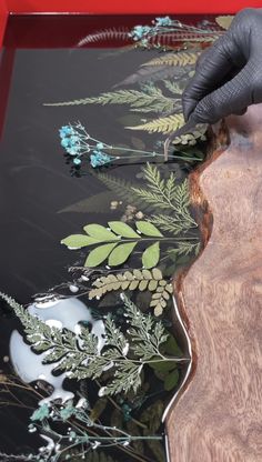 a person in black gloves is painting leaves on a piece of wood with acrylic paint