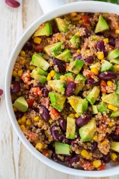 a white bowl filled with black beans, avocado and other vegetables on top of a wooden table