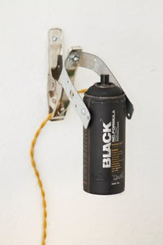 a black can is hanging on the wall with a yellow cord in front of it