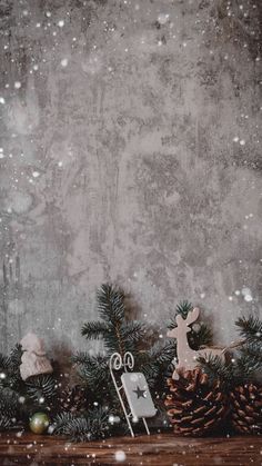 a christmas scene with pine cones and decorations on a table in front of a concrete wall