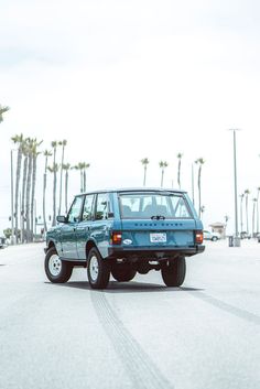 a blue car is driving down the street with palm trees in the backgroud