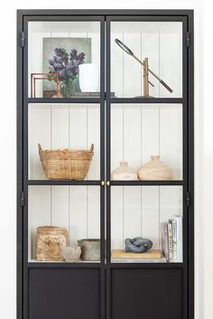 a black bookcase with glass doors and baskets on the bottom shelf is filled with books