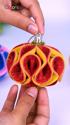 a hand holding a red and yellow ornament