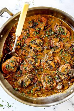 a pan filled with cooked shrimp and mushrooms on top of a white countertop next to a wooden spoon