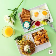 two white plates topped with breakfast foods next to a glass of orange juice on a green surface