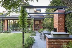 an outdoor kitchen and dining area with brick walls, green grass, and trees in the background