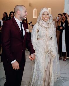 a man and woman in wedding attire standing next to each other with people taking pictures behind them