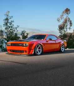 an orange sports car is parked on the side of the road with trees in the background