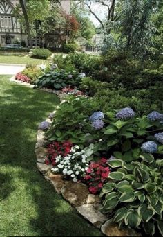 a garden filled with lots of flowers next to a lush green field and tree covered building