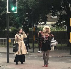 two women are walking down the street talking on their cell phones and one is holding a purse