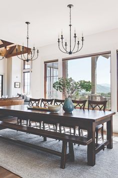 a dining room table and bench in front of a large window with chandelier