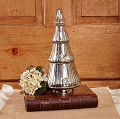 a silver christmas tree sitting on top of a book next to a vase with flowers