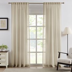 a living room with white curtains and a chair in front of the window that is open