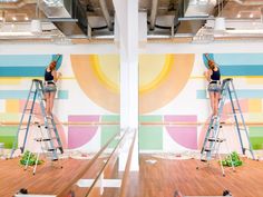 a woman standing on a ladder painting a wall