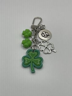 a green shamrock keychain sitting on top of a white table next to two clovers