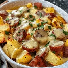 a white bowl filled with potatoes covered in cheese and sausages, garnished with parsley