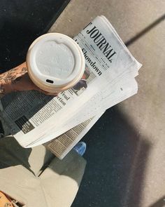 a person with tattoos is holding a cup of coffee and reading the news paper while sitting on a bench