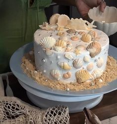 there is a cake that has shells on it and sand in front of the cake