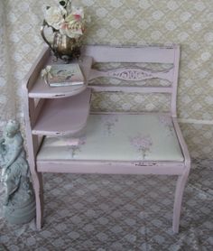 a pink bench with flowers on it next to a wallpapered wall and vase