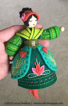 a hand holding a small doll in a green dress